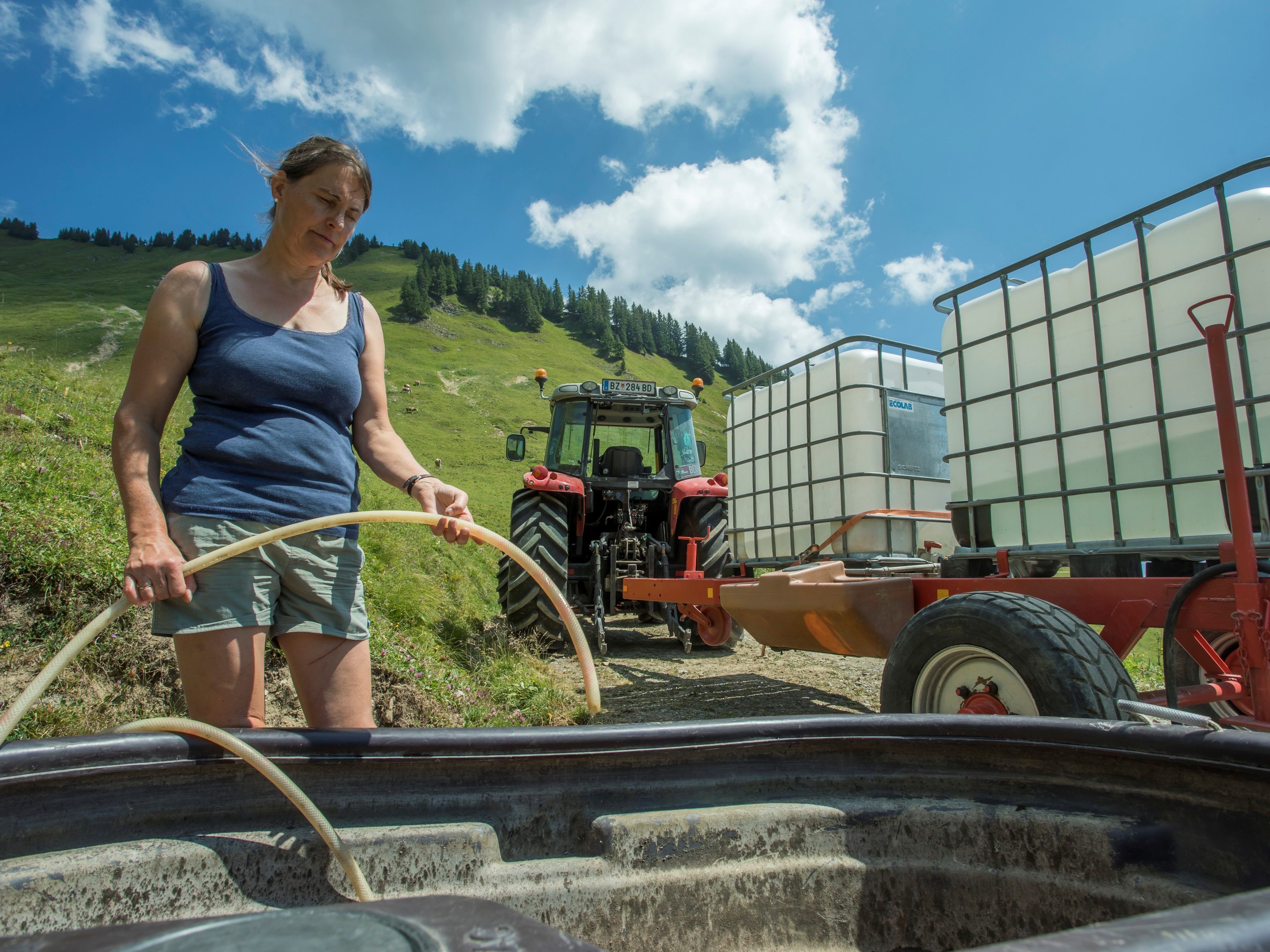 Hildegard Burtscher vor einem leeren Brunnen. Wasser muss in großen Behältern auf die Alpe geschafft werden.