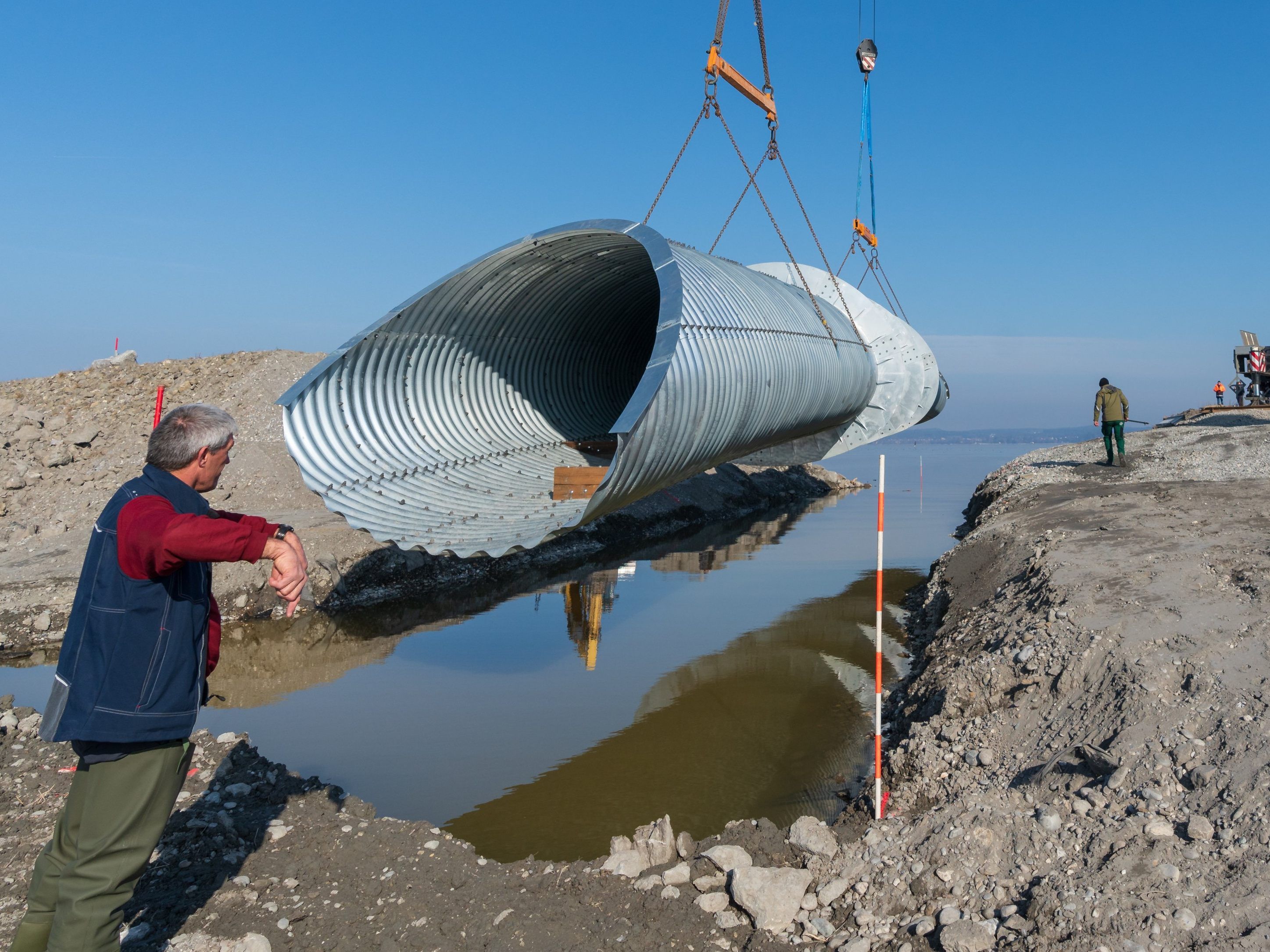 Mit zwei Telekränen wurde die Fischunterführung in das zuvor ausgebaggerte Loch am Rheindamm eingehoben.