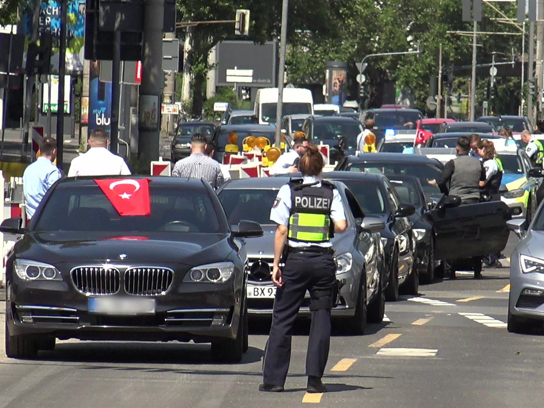 ine Polizistin steht vor den Fahrzeugen eines türkischen Hochzeutskorsos
