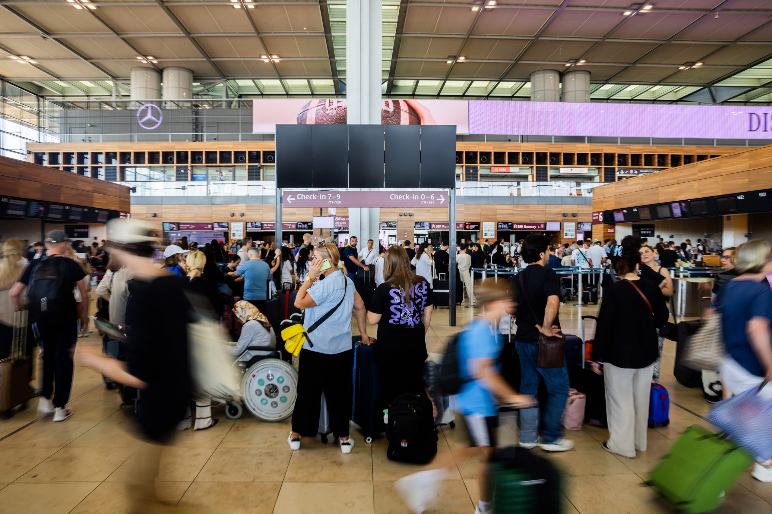 Zahlreiche Fluggäste warten am Hauptstadtflughafen BER vor einer schwarzen Anzeigetafel
