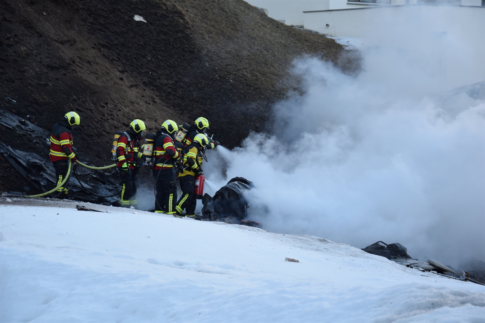 Feuerwehrleute löschen das brennende Wrack.
