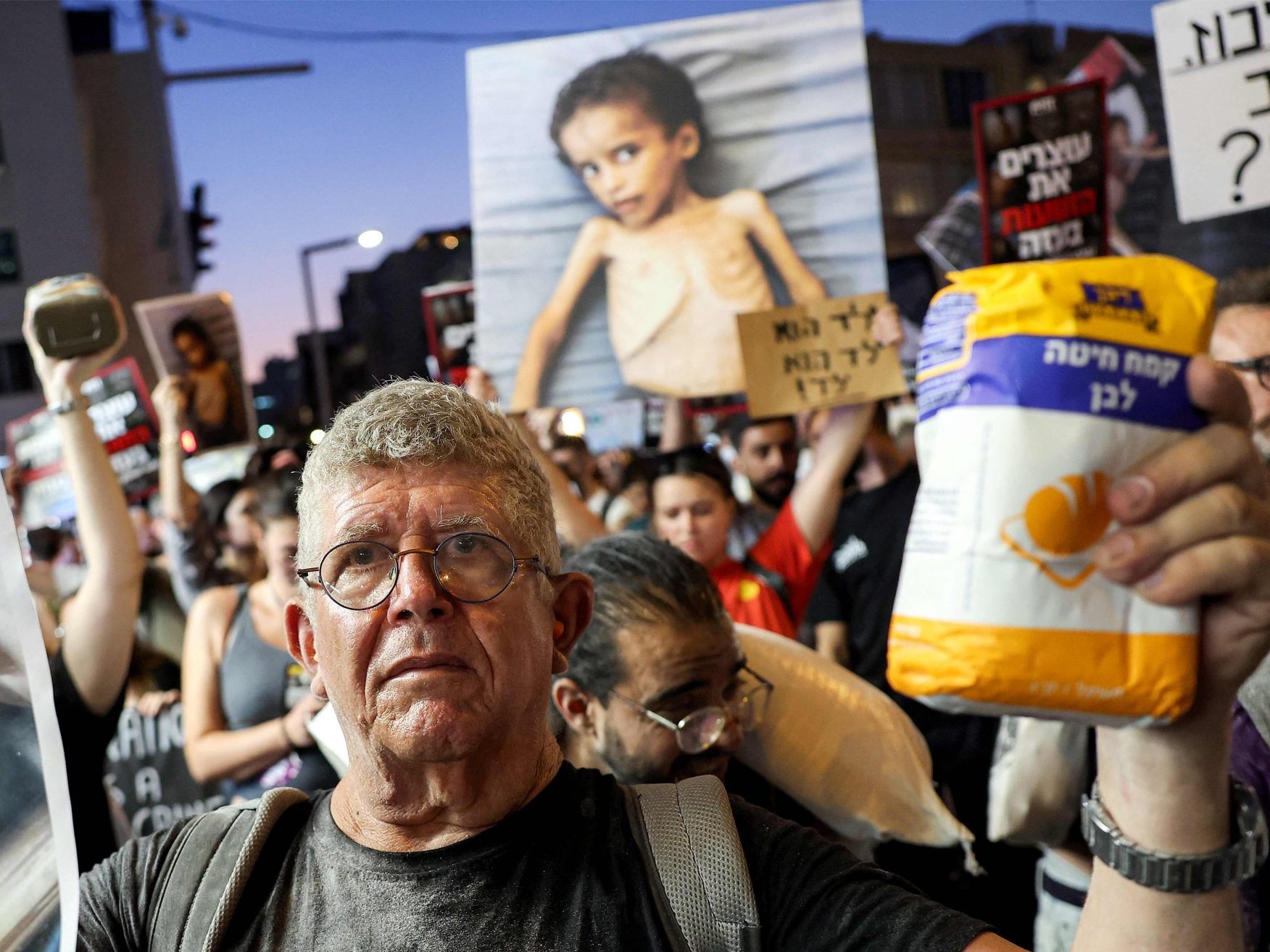 Ein israelischer Aktivist hält einen Sack Mehl und ein Bild eines unter Mangelernährung leidenden Kindes während eines Marsches zum Hauptquartier des israelischen Verteidigungsministeriums in Tel Aviv.