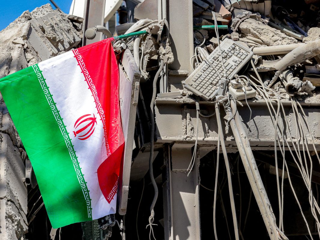Auf dem Bild sieht man eine Flagge des Iran. Sie hängt an einem zerstörten Gebäude in der Hauptstadt Teheran.